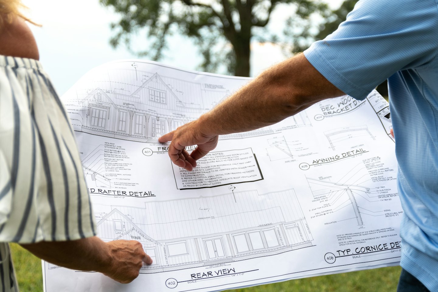 Two people discuss architectural house blueprints while standing outdoors.